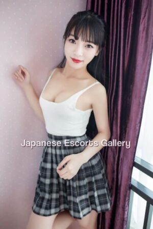 Vivi Small Teen Asian Escort poses in white vest and grey tartan skirt