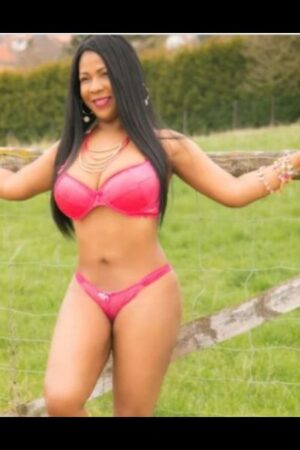 ebony Hull escort poses by a fence in a field