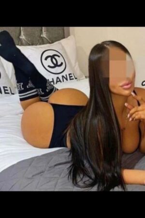 brunette Cambridge escort laid on a chanel themed bed