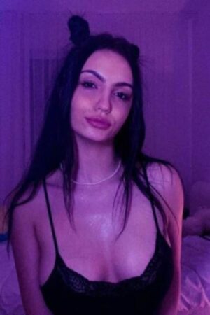 brunette Cambridge escort poses in UV light in her bedroom