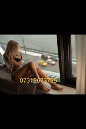 busty Reading escort posing by a high up window