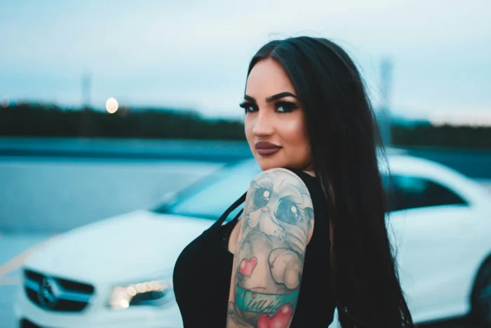 Brunette tattooed Ipswich escort posing in front of a car